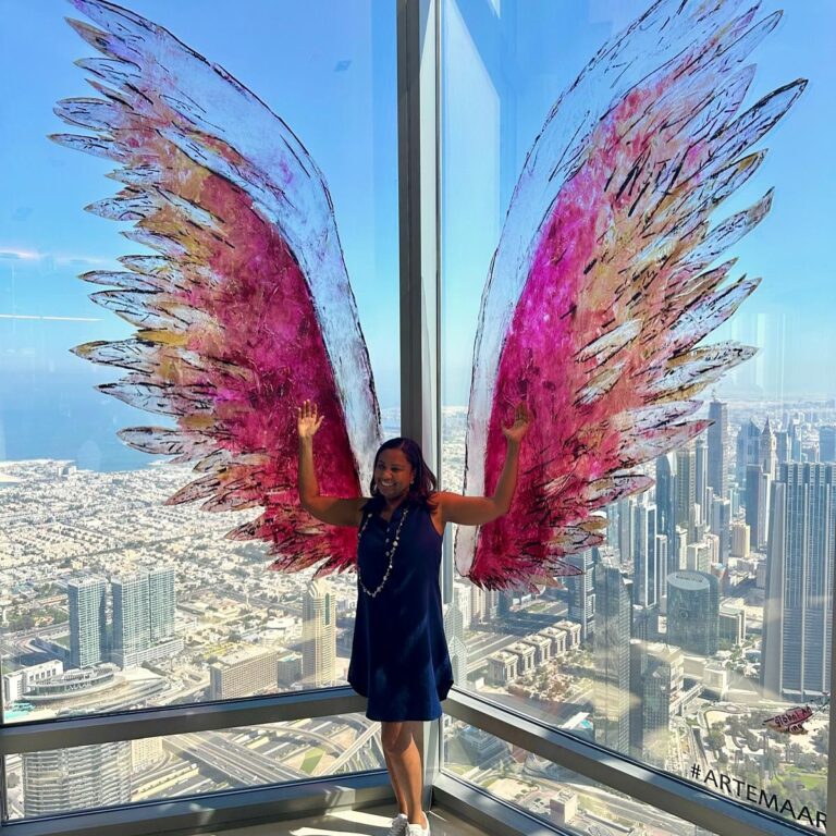 Viajera posando con unas alas de colores en un mirador sobre una ciudad de rascacielos